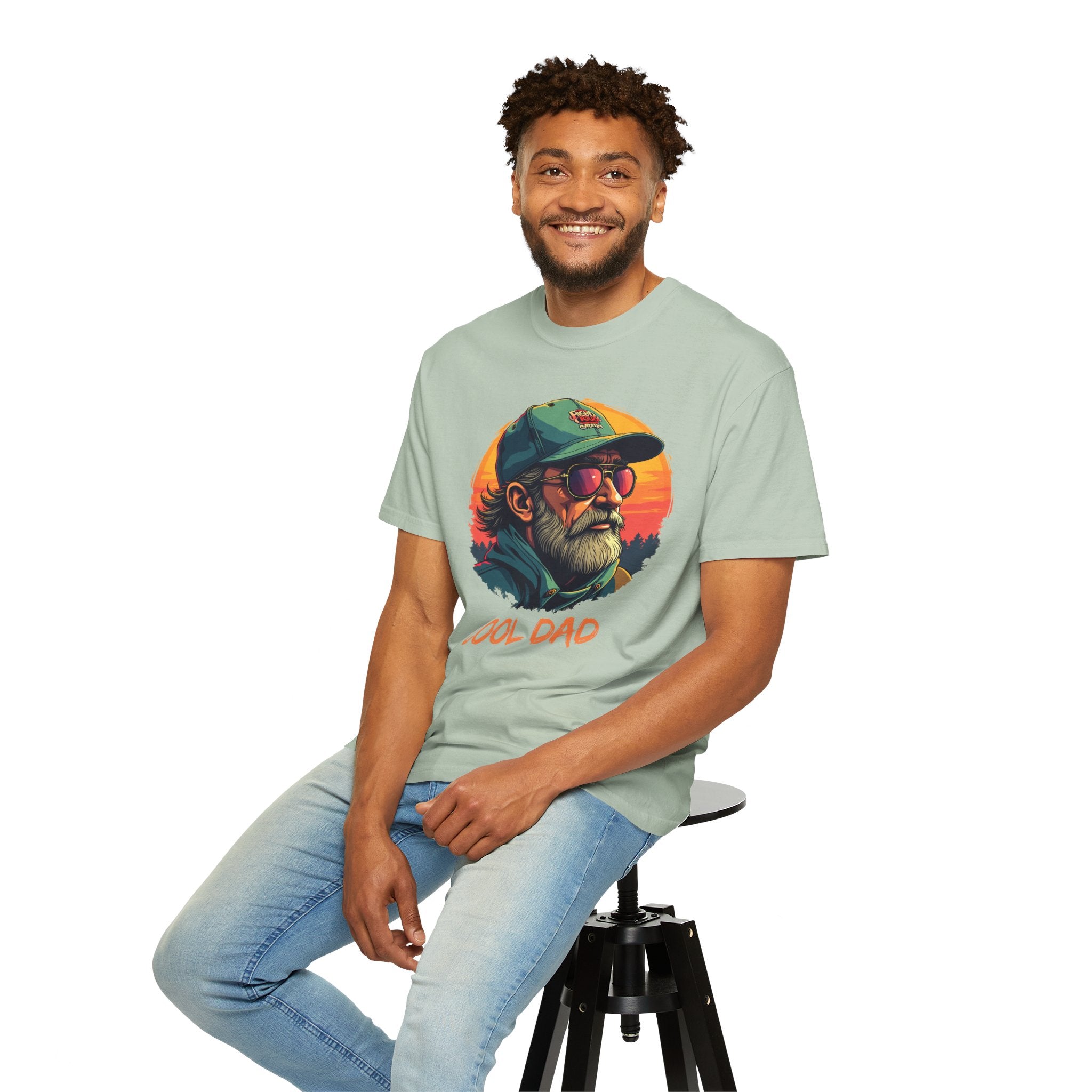 Man wearing a light green t-shirt with a graphic design sitting on a stool against a white background