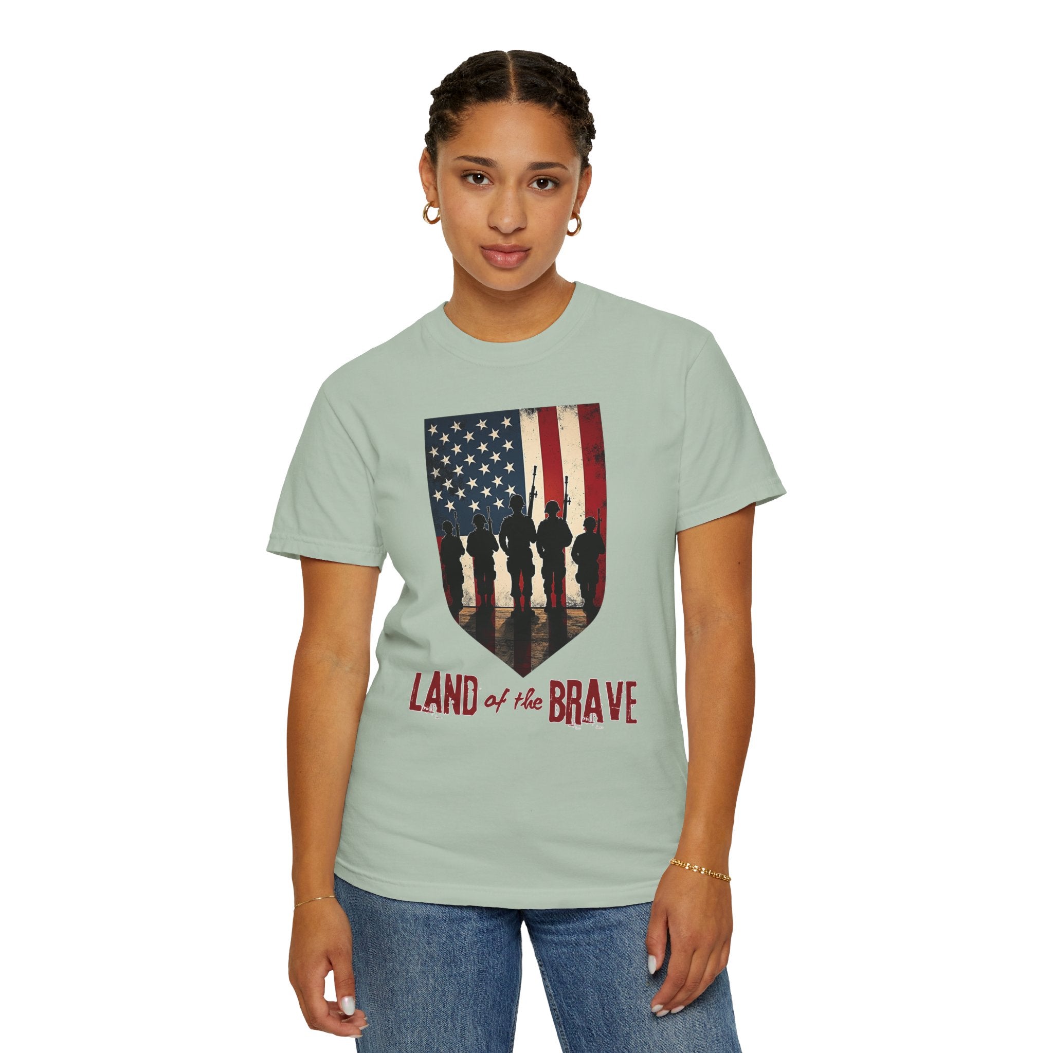 Person wearing a light green t-shirt with an American flag and silhouette design, text 'Land of the Brave' on a white background.