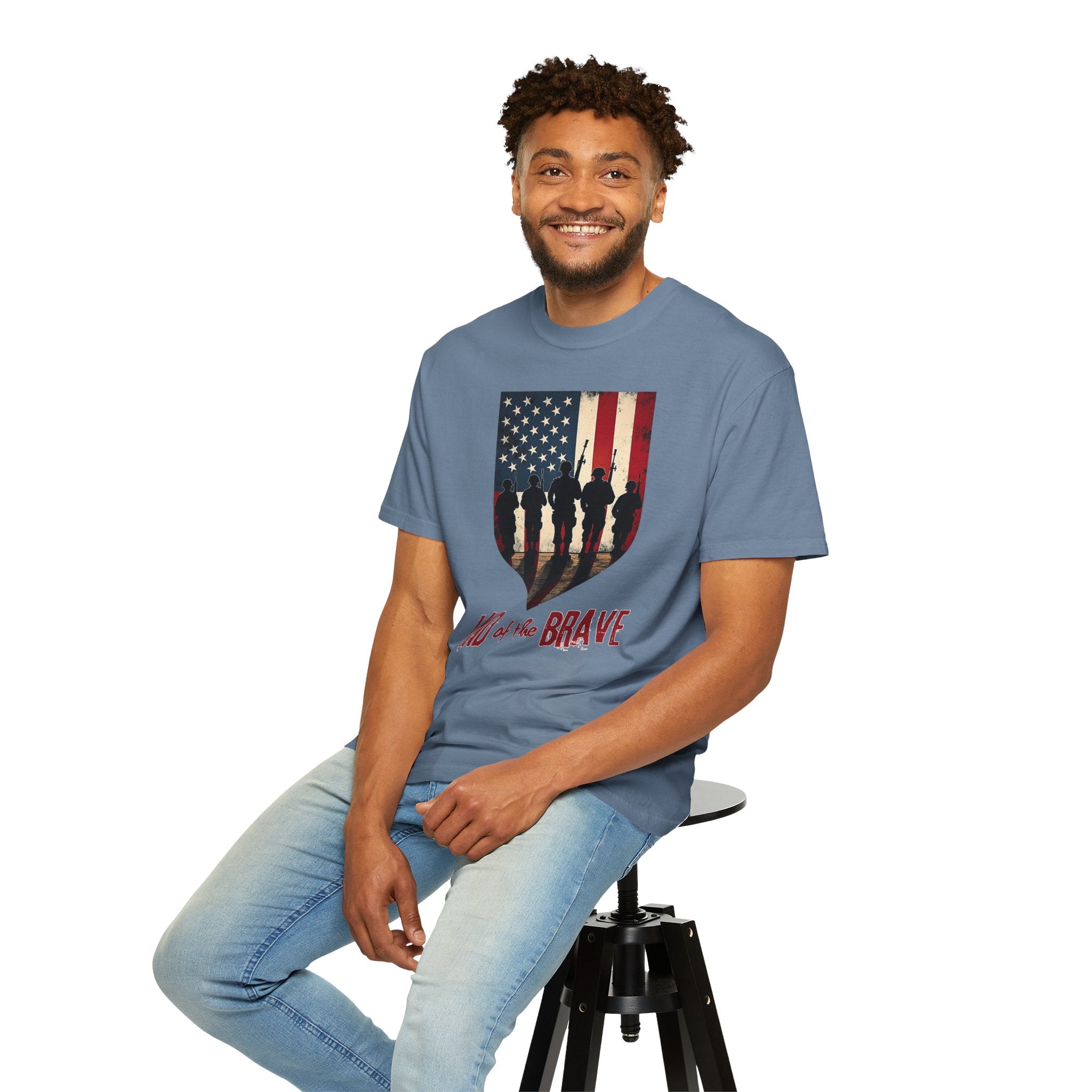 Man wearing a blue t-shirt with an American flag design, sitting on a stool against a white background.
